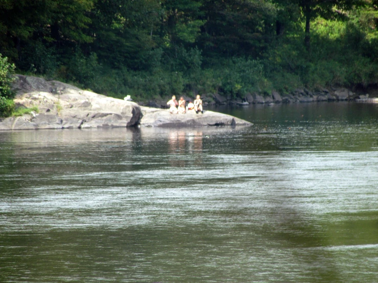 some people sitting on a rock by the water