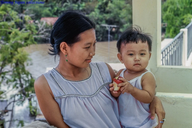 two women are holding an infant eating a piece of fruit