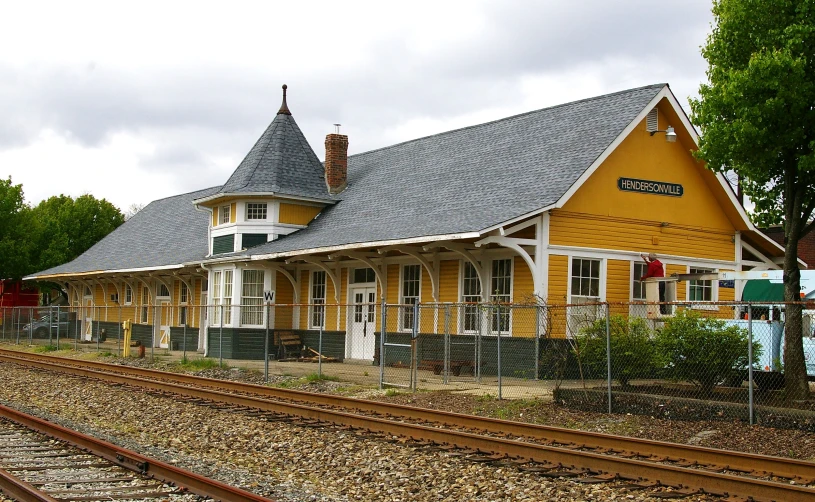 a yellow building with a black roof and two train tracks