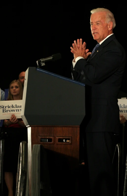 a man standing at a podium while holding his hands up