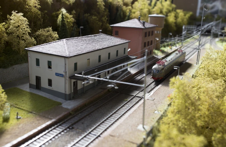 model train track with white building on right and trees in background