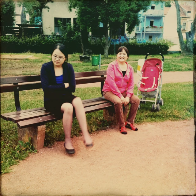 two women sitting on a park bench posing for a picture