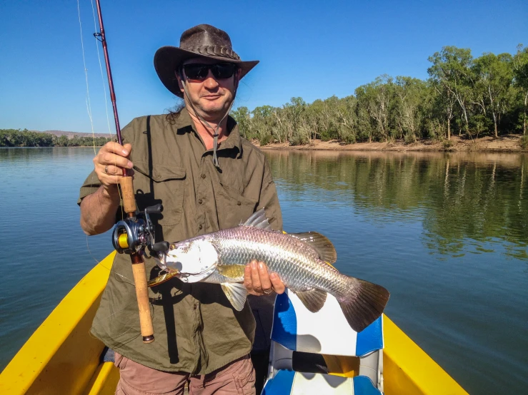 the man in the hat holds a fish while in a yellow boat