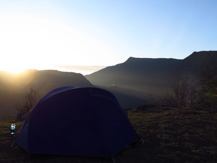a blue tent with the sun peeking through and mountain in the background