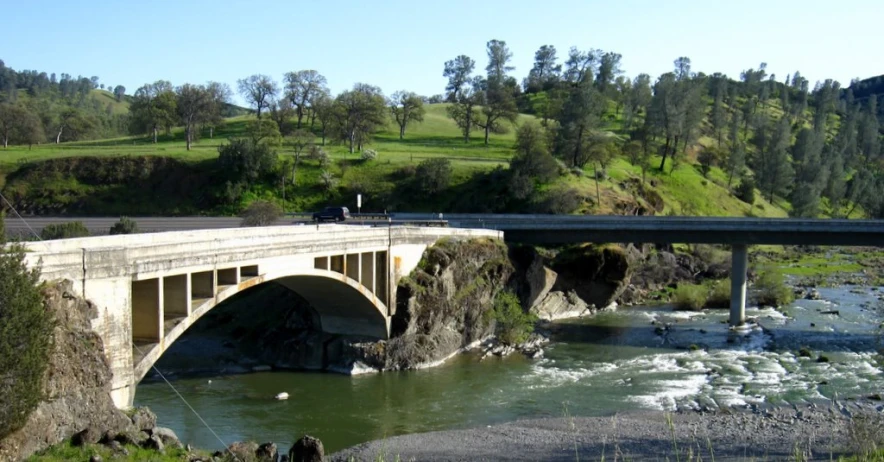 a bridge over some water near a field and a hill