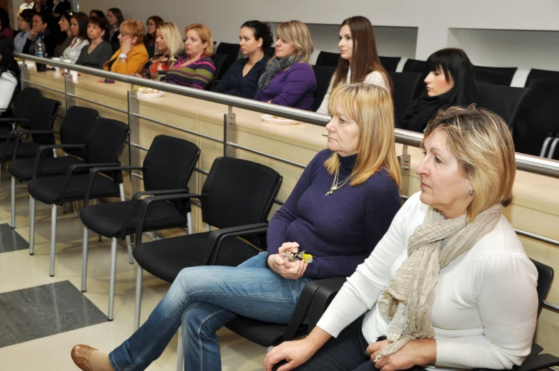 two women at a lecture hall with people watching