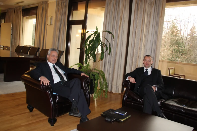 two men in black suits sitting down and standing