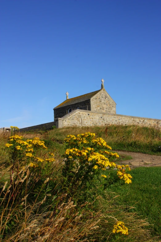 a stone house on the hill has flowers in front of it