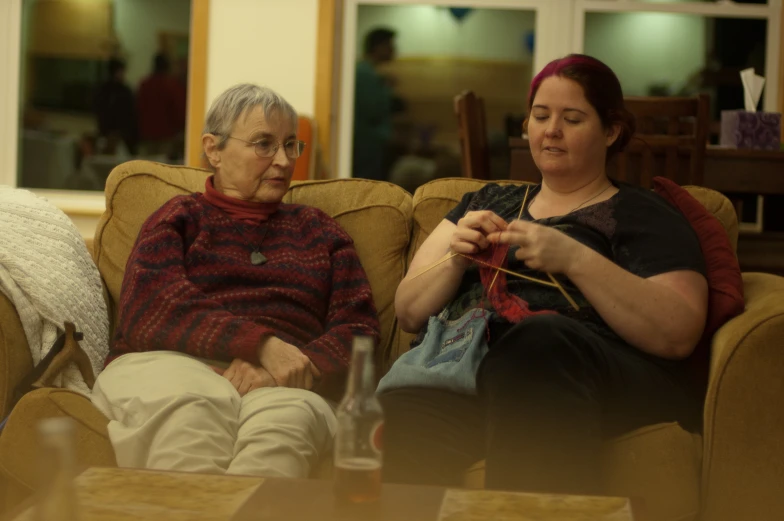 two women sit on the couch with knitted items