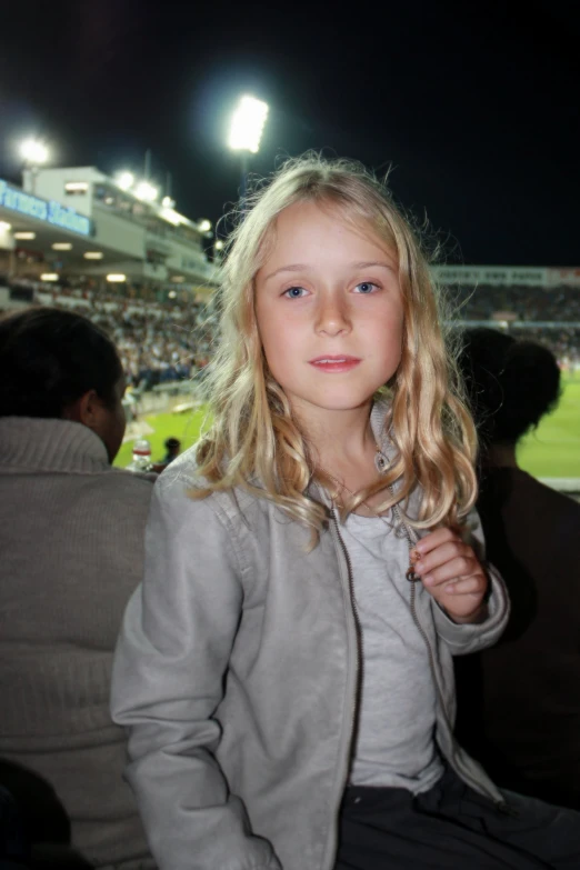 a girl with a jacket on sits in a stadium