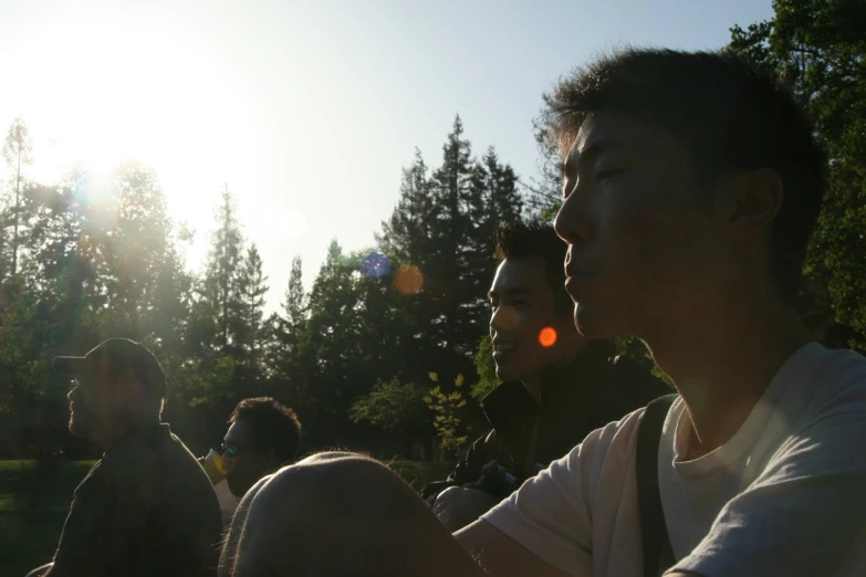 a group of men sitting in a park with the sun behind them