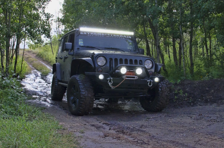 a green jeep driving on dirt road next to trees