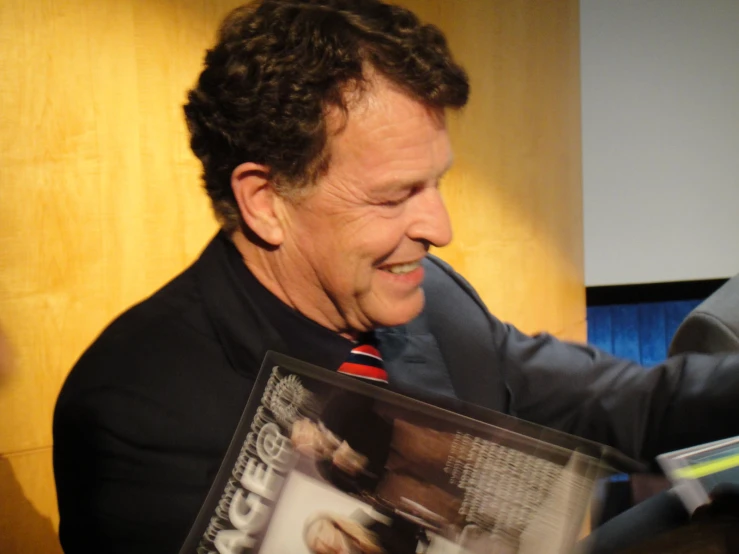 a smiling man wearing a suit and tie holding up a magazine