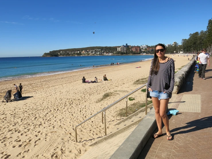 woman in sunglasses on beach standing next to railing