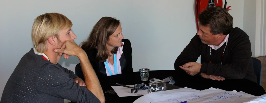 three people at a round table talking, looking at papers