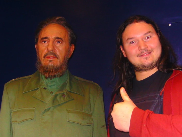 a man with long hair giving the thumbs up next to an older gentleman in green