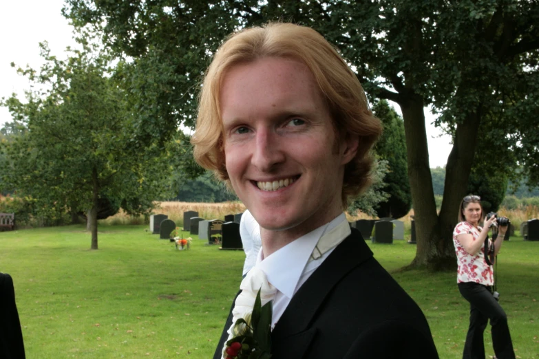 a man wearing a suit and flower stands on the grass