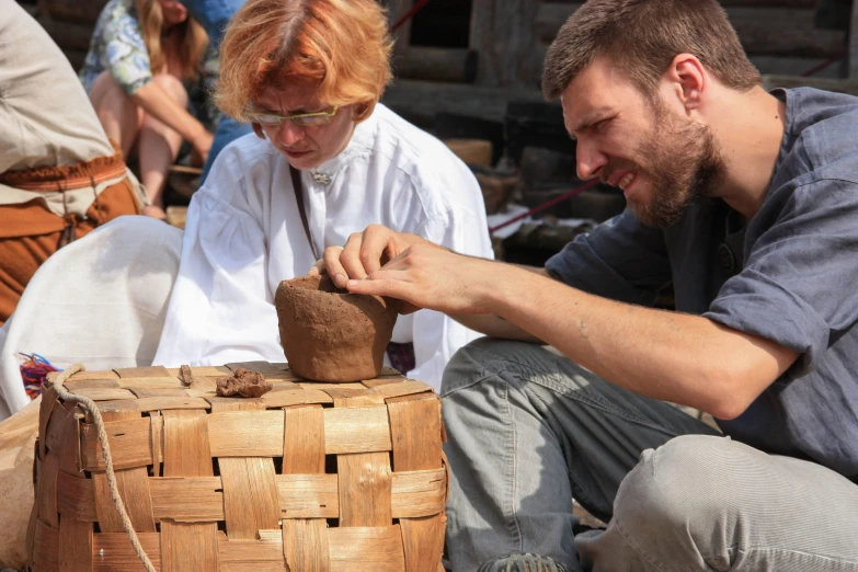 a woman sitting next to a man working with clay