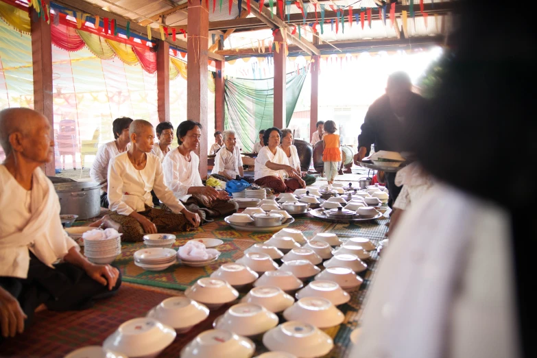 several people sitting on the ground in front of various foods and drink plates