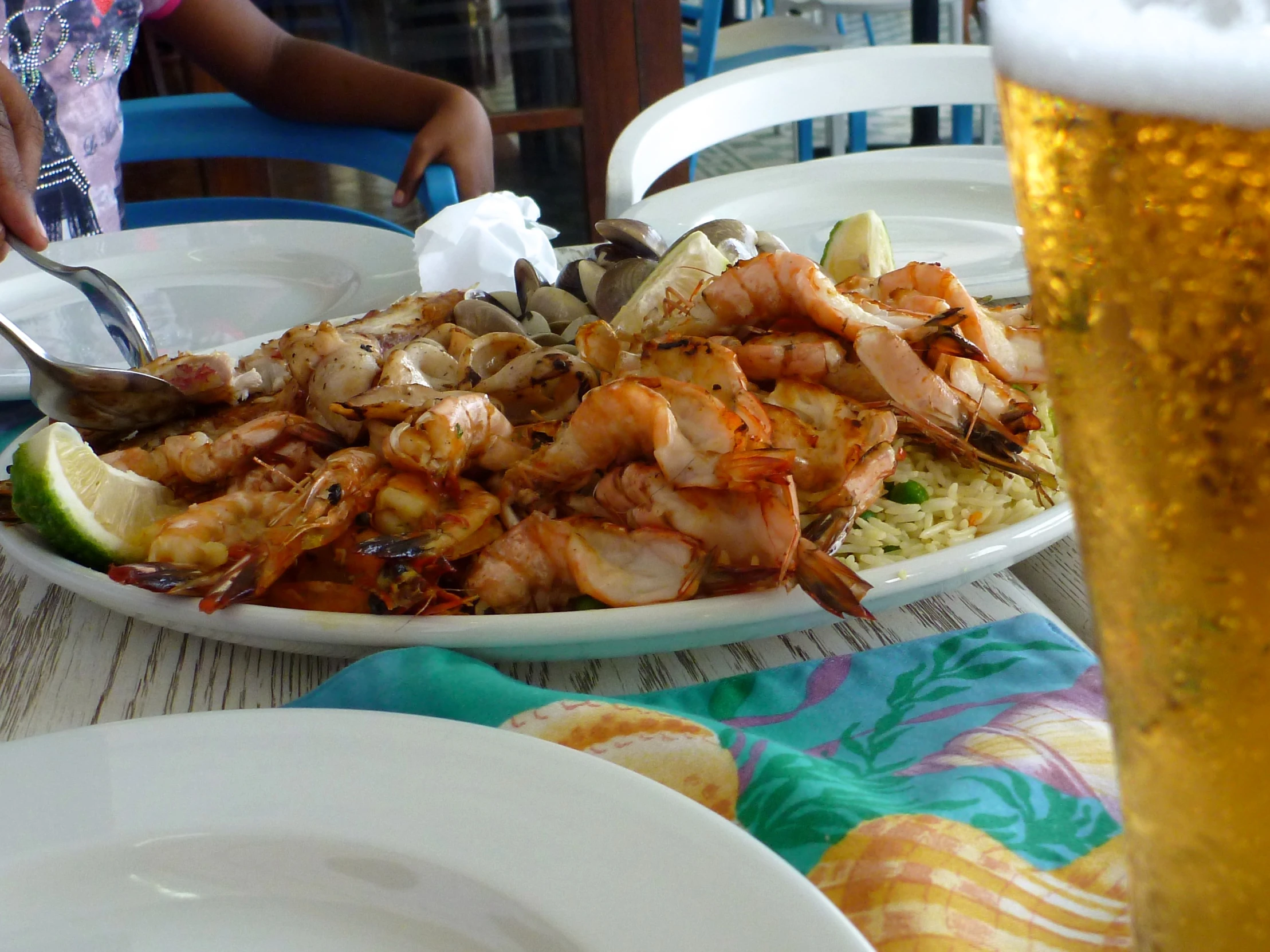 two plates of shrimp, rice and vegetables with a glass of beer