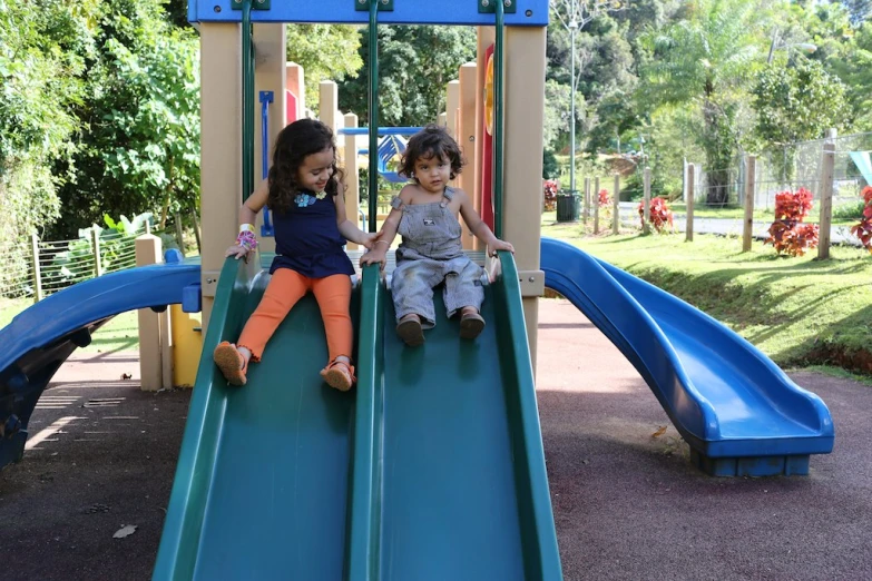 two young children sitting on blue slides in a park