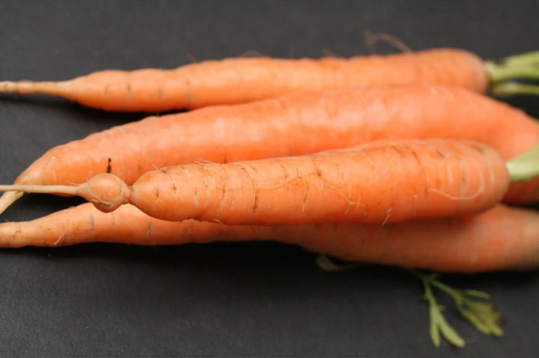 two large, bright, ripe carrots sitting on a black surface