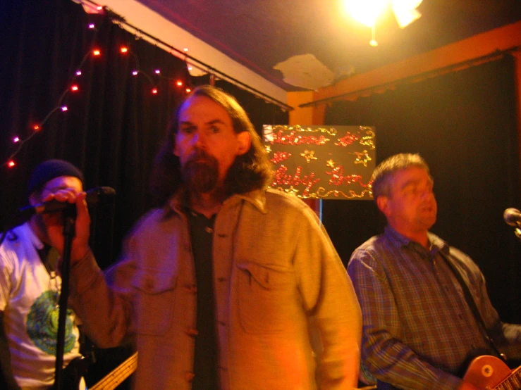 three men stand in front of a microphone in a band