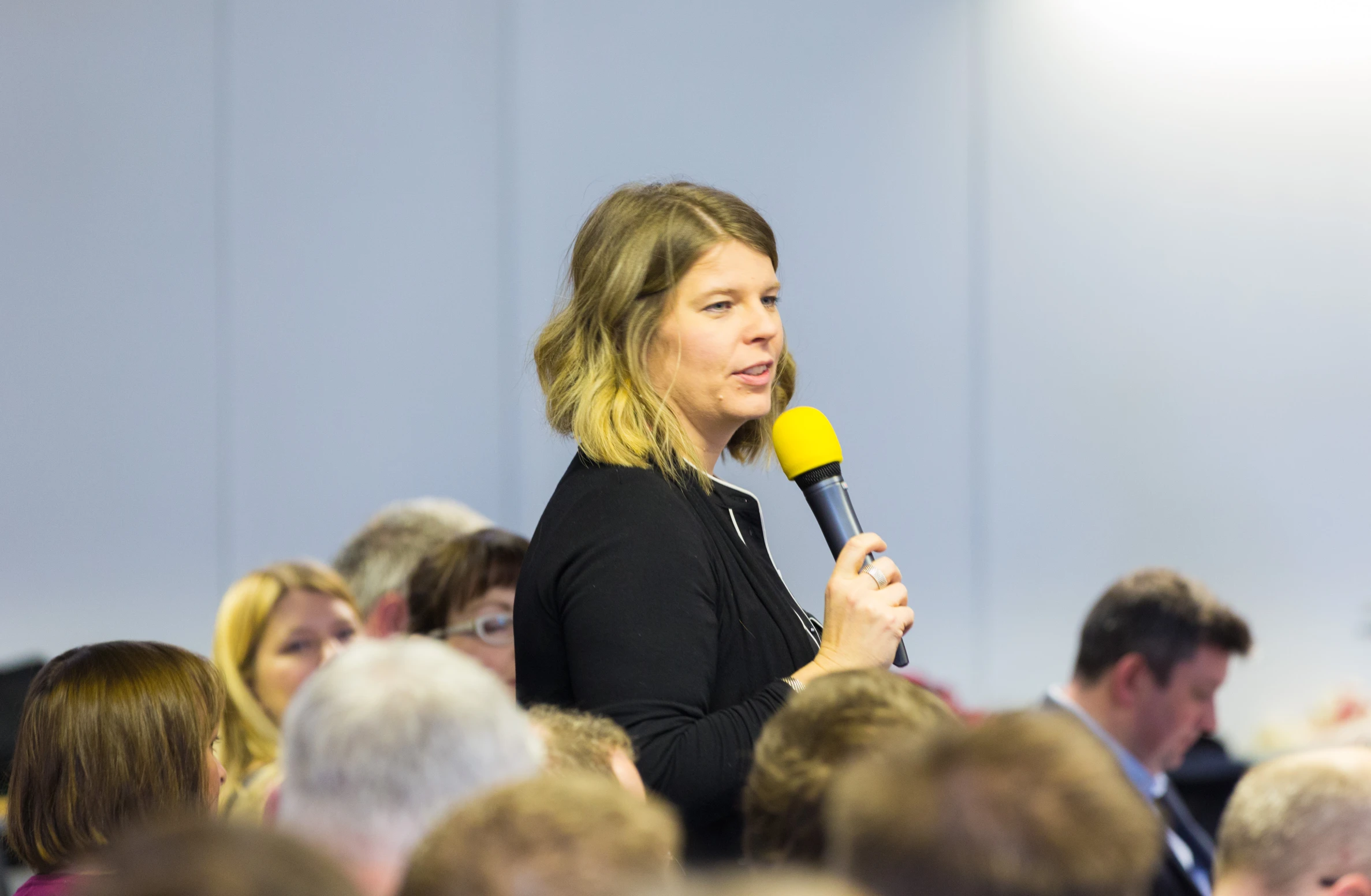 a woman speaking at an event in a room full of people