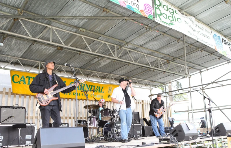 three guys playing guitar on stage under a covered structure