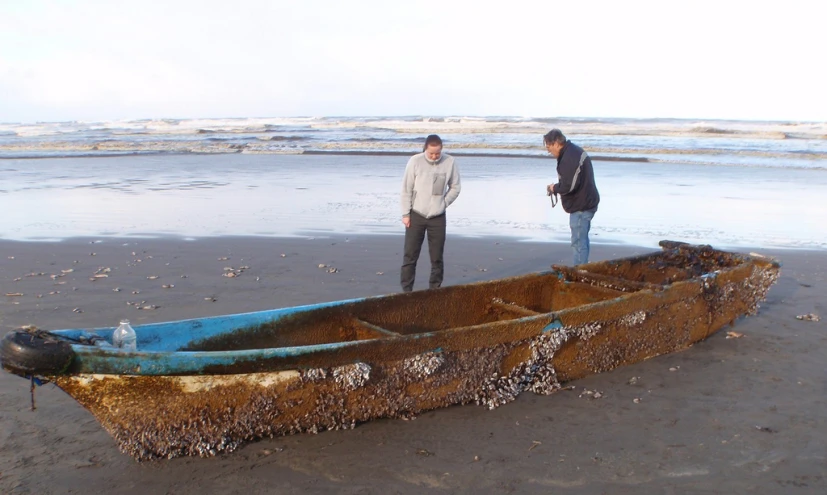 two people standing on top of a boat on a beach