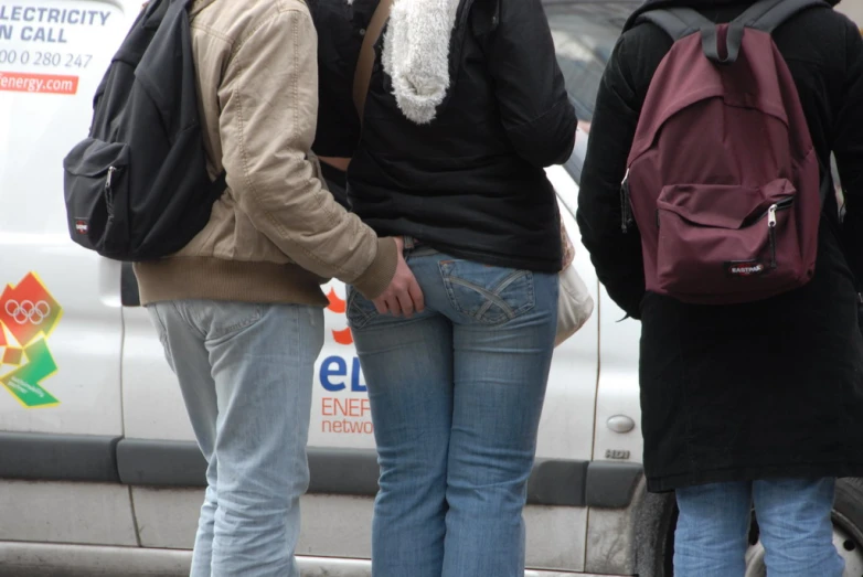 some people wearing coats and backpacks standing in front of a van