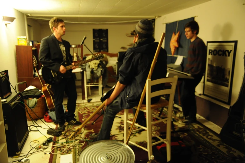 three men are in a room with one playing guitar and the other singing