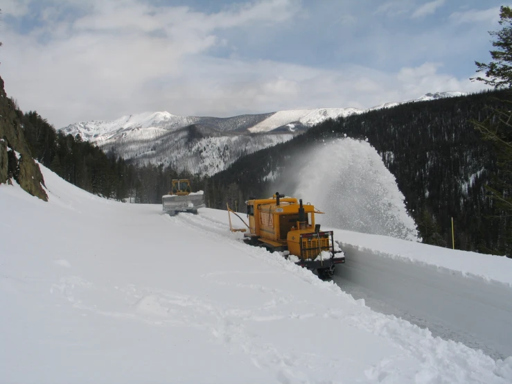 two snowplows are in the snow near a large snowy mountain