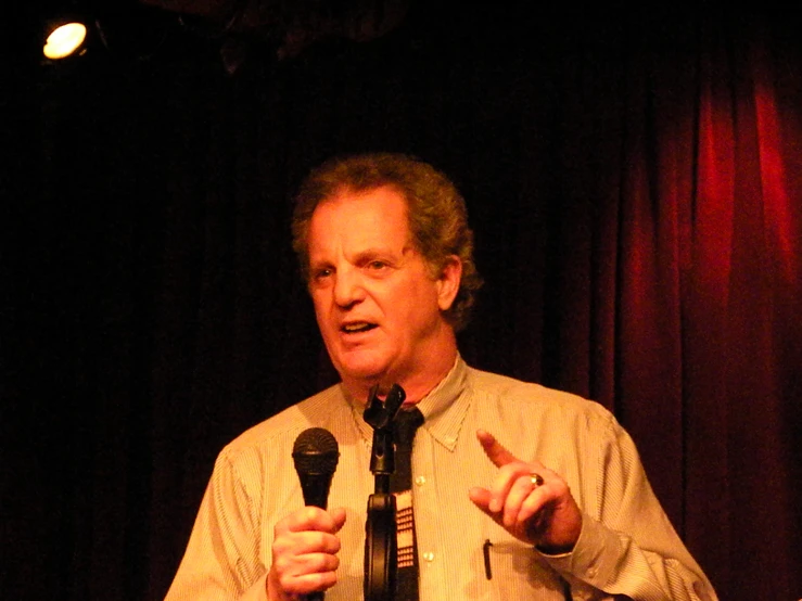 a man in dress shirt and tie with microphone giving a speech