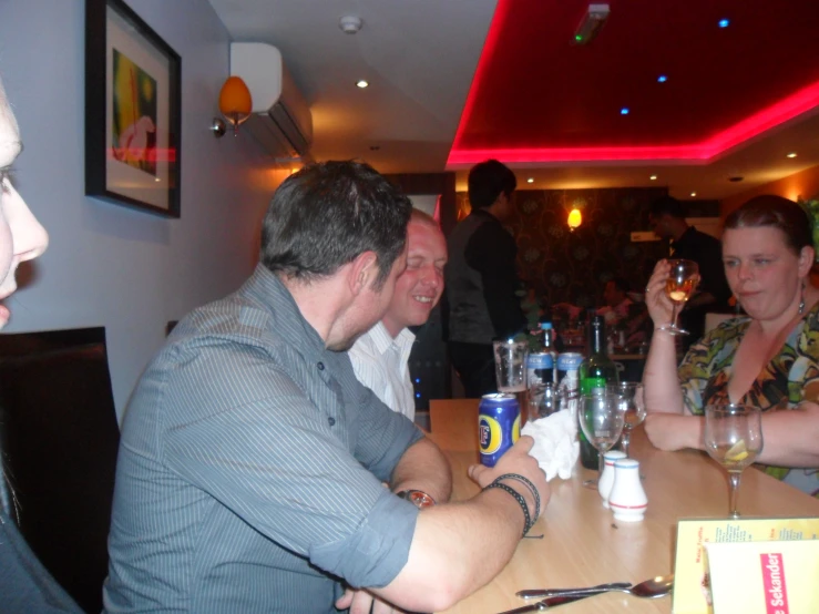 two women smiling while the man in the blue shirt sits at a table