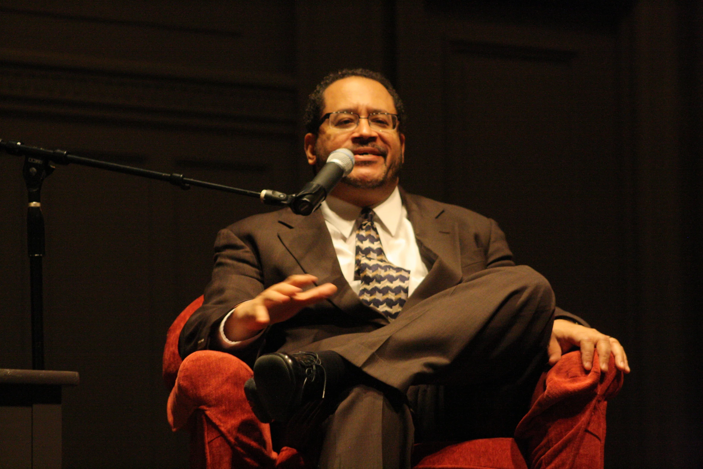 a man with glasses and a tie sitting in a chair
