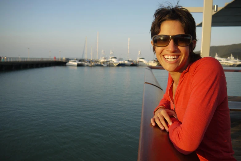 a woman wearing sunglasses poses for the camera near boats