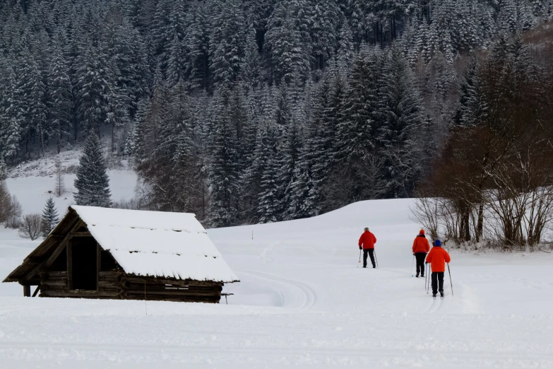 three people walking across a snow covered field with a cabin in the background