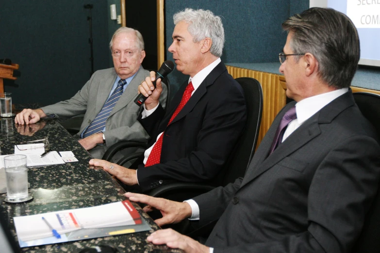 four men seated at a table with microphones and books