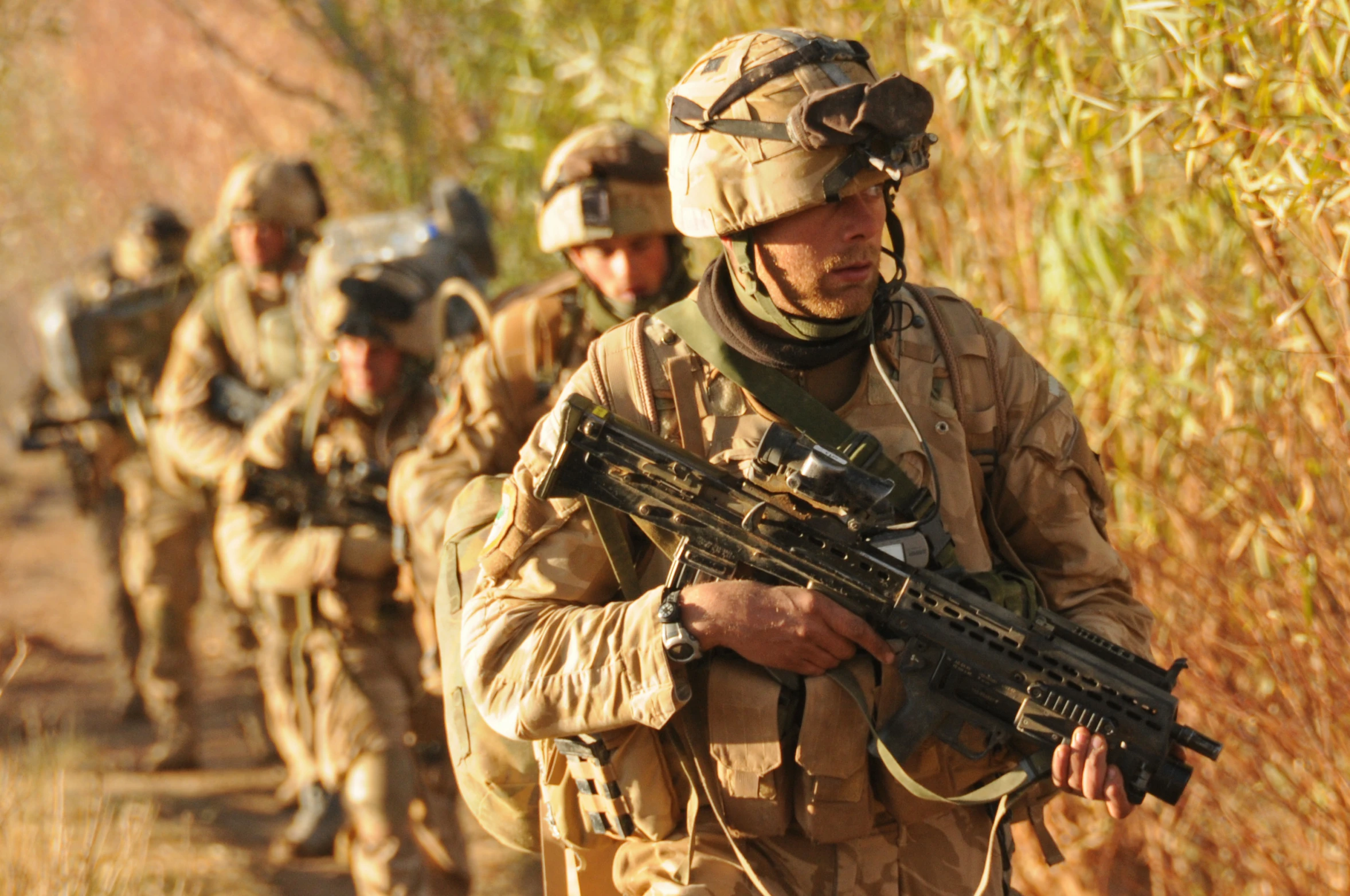 a group of soldiers carrying rifles down a dirt road