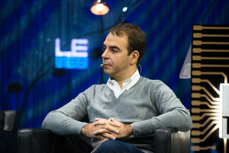 a man sits on a chair in a studio with a blue backdrop