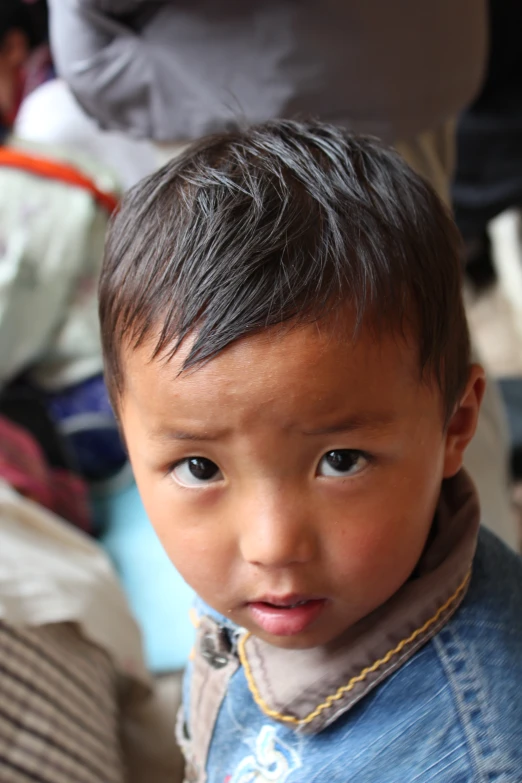 a small, baby boy with light blue eyes wearing a denim bib