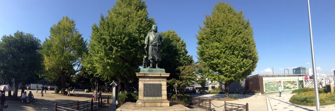 a statue on a pedestal in a park area with a clock tower