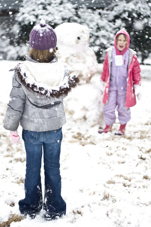 a small child stands in the snow, next to a large snowman