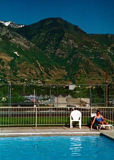 a man sitting on a white chair near a pool in front of a mountain