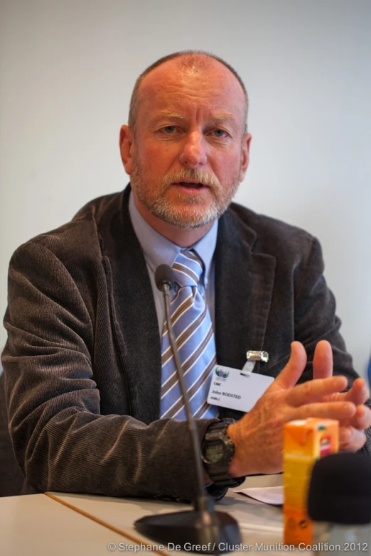 a man sits at a table with his hand out to his chest