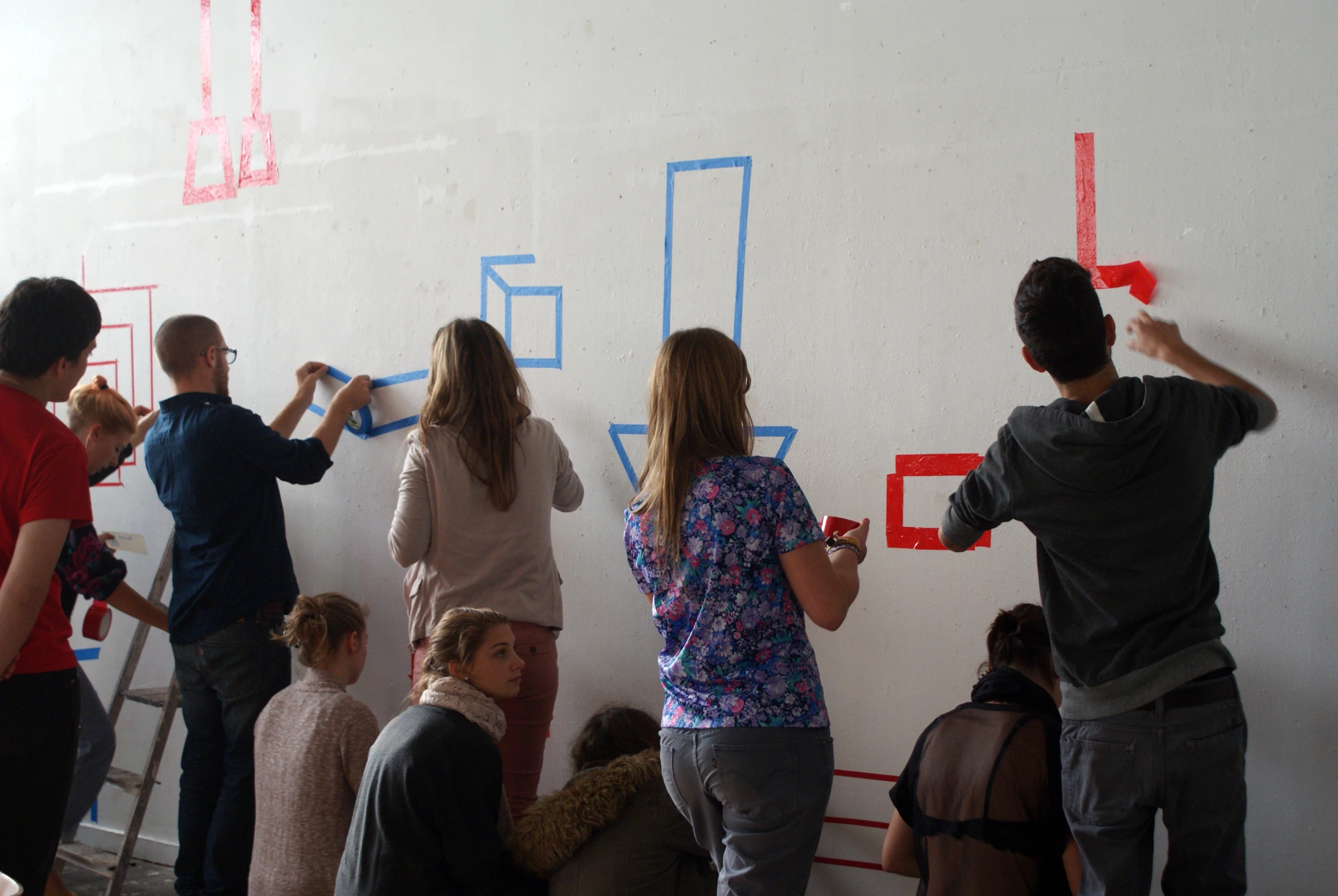 a group of people painting the wall with large red tape