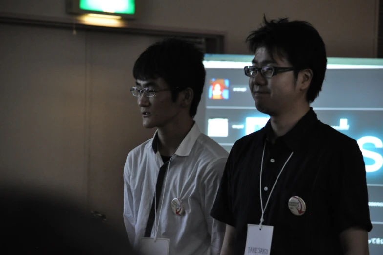 two men standing next to each other with a sign in the background