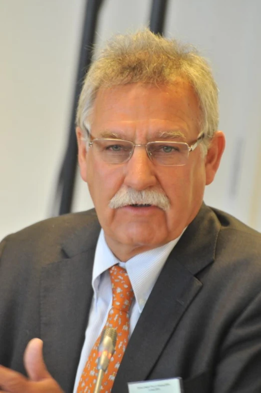 a man wearing a business suit with a small patched tie and glasses