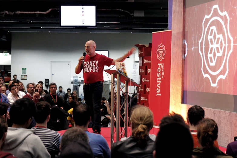 a man stands on stage speaking to an audience